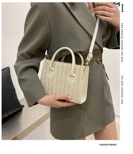 Detail view of a woven straw crossbody bag with white leather handle and gold hardware
