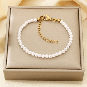 Detail of white round pearl bracelet with golden adjustable clasp on champagne silk fabric