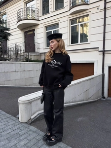 Streetwear style black sweatshirt featuring white varsity lettering print in an outdoor setting