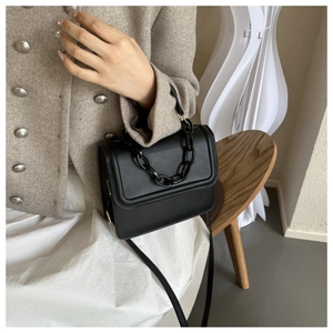 Detail of a black square leather handbag featuring a stylish thick chain decoration