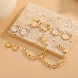 Elegant gold and silver zircon geometric hoop earrings displayed on a minimalist stone