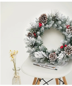 Detail of green PE needles with red berries and snow-dusted pine cones on a Christmas wreath