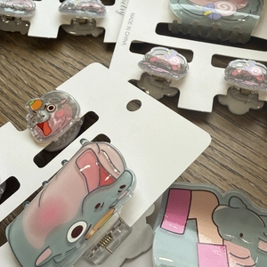 Detailed flat lay of acrylic cartoon hippo hair clips with candy charms on wood surface