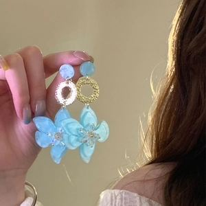 Detail of light blue resin flower earrings with gold textured rings on a model