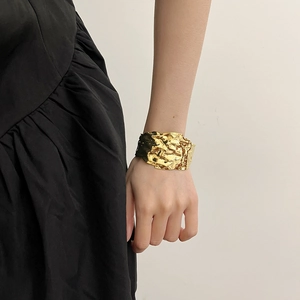 Detail of gold-plated wide cuff bracelet featuring irregular hammered texture and pleated design