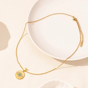 Close-up of golden Evil Eye pendant with blue crystal and lobster clasp on a ceramic plate