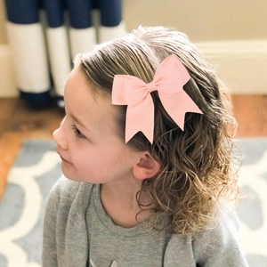 Pink grosgrain ribbon bow hair clip worn by a young girl with blonde curly hair