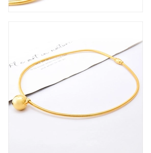 Close-up of a minimalist golden ball pendant on a sleek metallic hose choker necklace