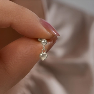 Macro detail of a minimalist silver heart pendant earring held to show scale and texture