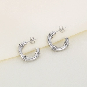 Gros plan de boucles d'oreilles argentées en C avec zircons blancs pavés sur du tissu