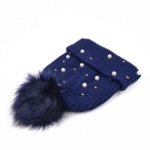 Dettaglio berretto in maglia blu navy con pompon in pelliccia, perle bianche e perline oro