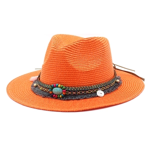 Detail van feloranje strohoed met turquoise kralen en een zilveren muntpendel
