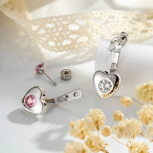 Silver heart earrings with pink and clear gemstones on a white lace background