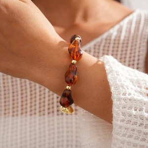 Gros plan d'un bracelet en résine ambrée aux perles irrégulières porté au poignet