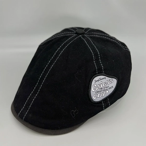Close-up of black retro beret with white contrast stitching and side woven label
