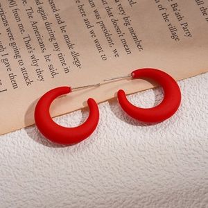 Macro detail of matte red acrylic C-shape earrings on a vintage newspaper background