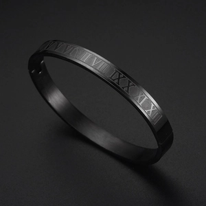 Detail of black metal cuff bracelet with engraved Roman numerals on dark background