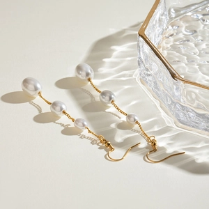 Elegant stainless steel long pearl tassel earrings with gold chains on a display tray