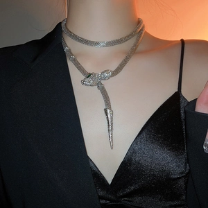 Detailed view of silver snake-shaped necklace with crystals and green stone eyes on model