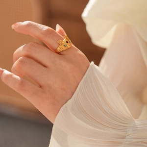 Detail of 24k gold plated fox ring with red and green gemstone eyes on model's finger