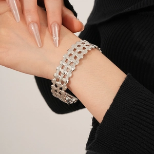 Detailed shot of silver wide-band geometric mesh bracelet worn over a black sweater sleeve