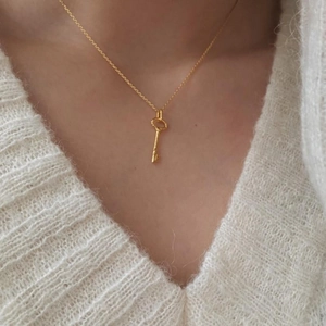 Detailed close-up of a vintage golden key pendant necklace worn on a white sweater