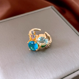 Close-up of golden geometric ring with blue and green crystals on silk fabric