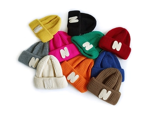 Stack of colorful knitted beanies for kids with N letter patch in various vibrant shades