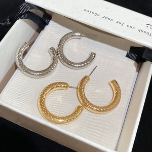 Detail of C-shaped gold and silver earrings with textured finish in a gift box