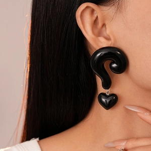 Detail showing oversized black glossy question mark earrings with a 3D heart pendant charm