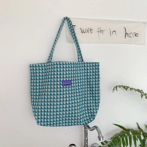 Detail of blue and white checkered wool tote bag hanging on a white wall with minimalist decor