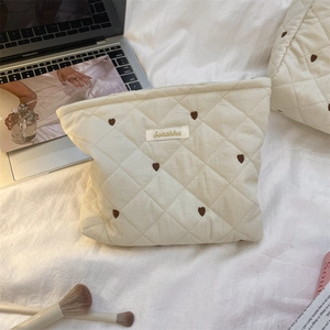 Nahaufnahme der beigen gesteppten Kosmetiktasche mit Herzstickerei und Logo