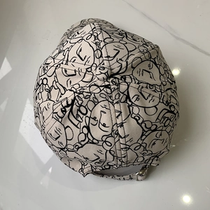 Close-up of adjustable metal buckle and cartoon face print on beige cotton baseball cap