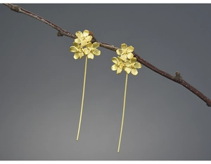 Macro shot of gold floral long drop earrings hanging on a natural wooden branch