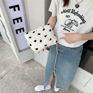 Close-up of white plush tote bag with black heart pattern held by a model