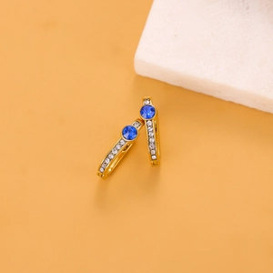 Detail view of golden hoop earrings with blue round gemstone and small white crystals
