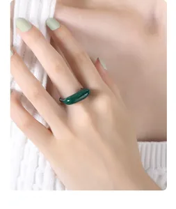 Close-up of minimalist dark green ring on index finger with matching green manicure