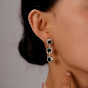 Close-up of elegant triple flower drop earrings with emerald green crystals and silver finish