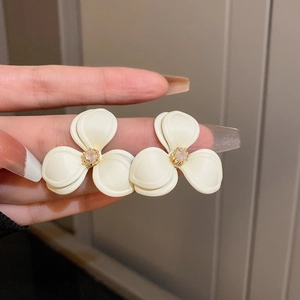 Close-up of creamy white three-petal flower stud earrings with champagne center crystal