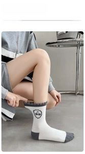 Détail de chaussettes en coton blanc avec bord gris, logo cerise et revers élastiques à volants