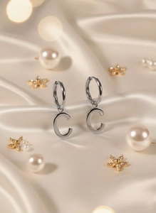 Detailed view of silver letter C pendant earrings on elegant champagne silk background