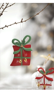 Detail of red Christmas gift bag ornament with green bow and golden bells hanging on branch
