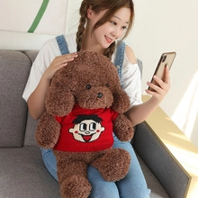 Brown teddy bear plush in red knit sweater shown in a cozy home lifestyle scene