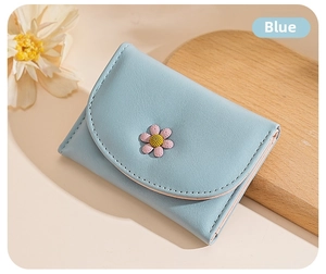 Close-up of light blue trifold wallet with delicate daisy flower and stitched texture