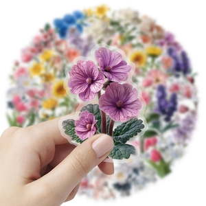 Close-up of a hand holding a purple floral PET sticker against a blurred flower collection