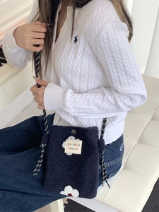 Navy blue plush floral crossbody bag with woven strap shown in a minimalist setting