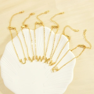 Detail of letters U to Z on 18K gold plated chains displayed in a seashell plate
