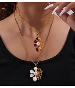 Dettaglio collana doppia a catena ritorta dorata con ciondoli a fiore e perle in smalto