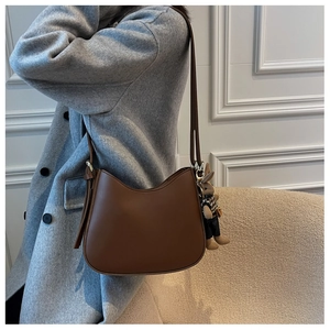 Detail of dark brown leather shoulder bag with adjustable strap and plush bear charm