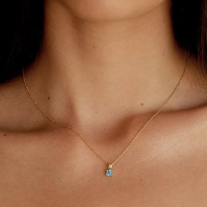 Detail of a minimalist gold S925 silver necklace with a blue birthstone on a model's neck
